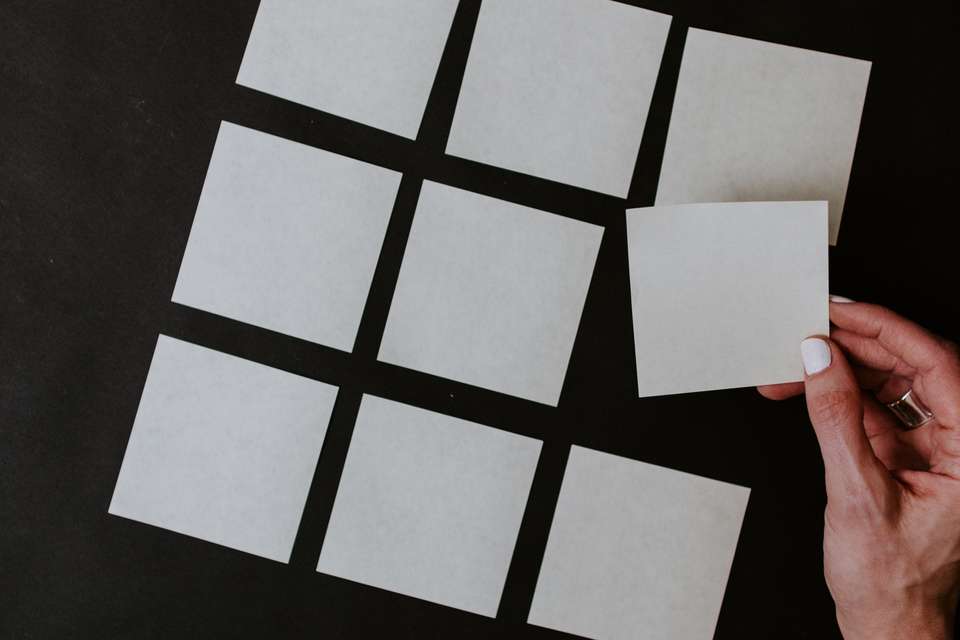 A hand sorting a piece of paper into a collection of other pieces of paper on a table.